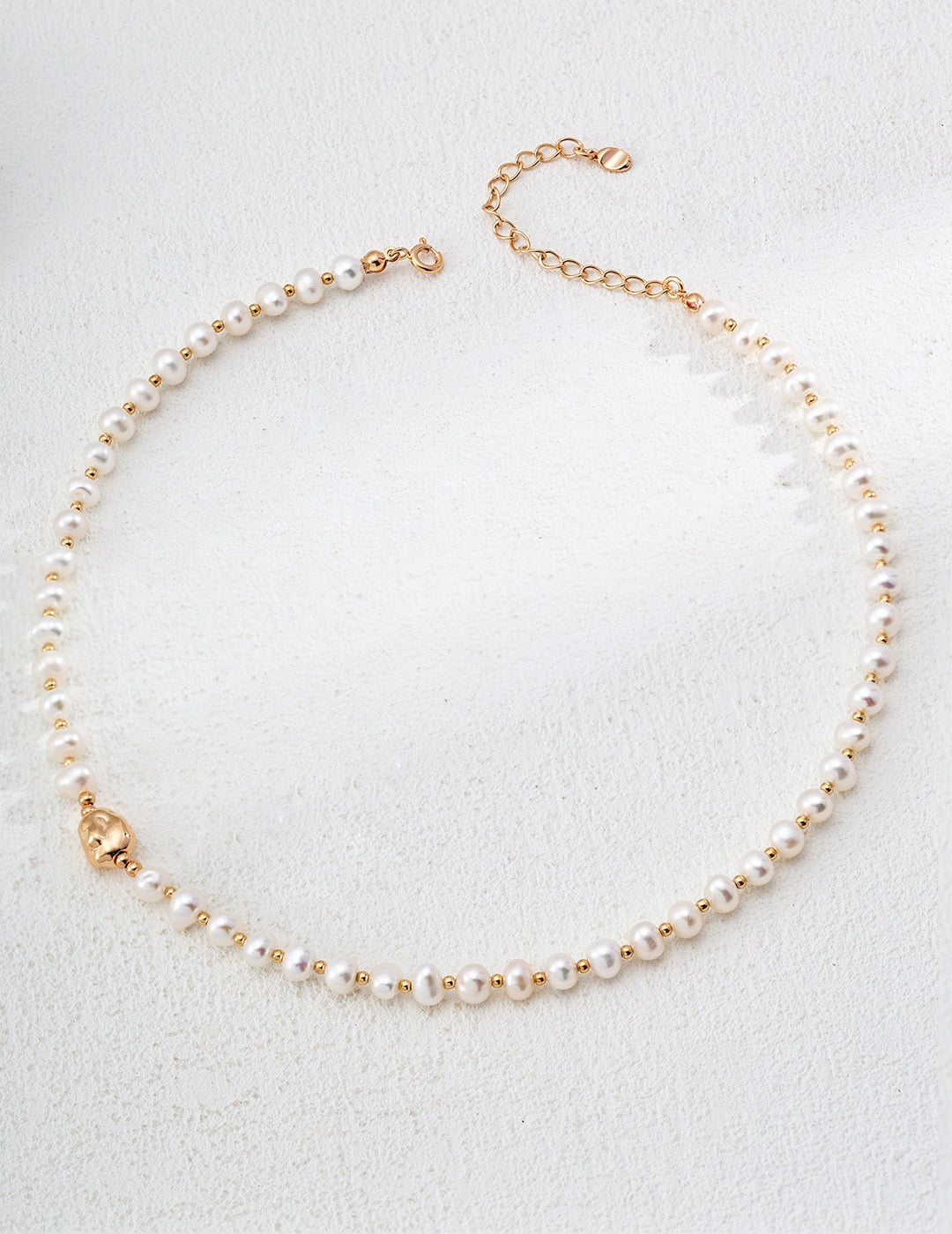 Natural freshwater pearl necklace with 18K gold and white gold plated 925 silver beads on white textured background