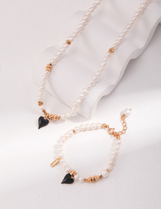 Natural pearl necklace and bracelet set with black enamel heart charm and gold accents on white background