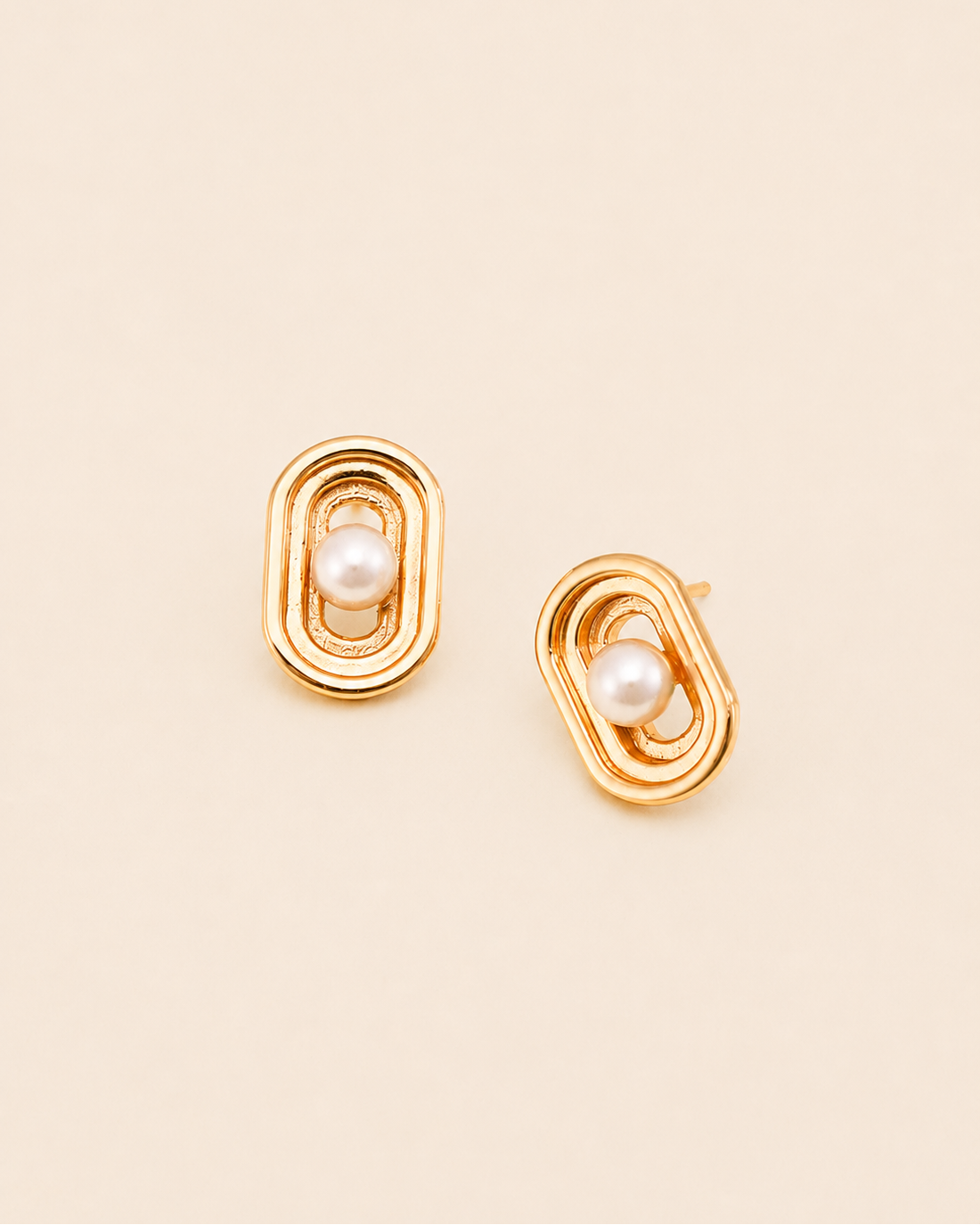 Elara Pearl Stud Earrings featuring a modern geometric frame and luminous pearl centerpiece in polished gold finish.