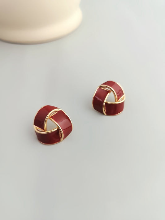 Gold and red enamel glaze knot stud earrings with modern twisted design on a light background.
