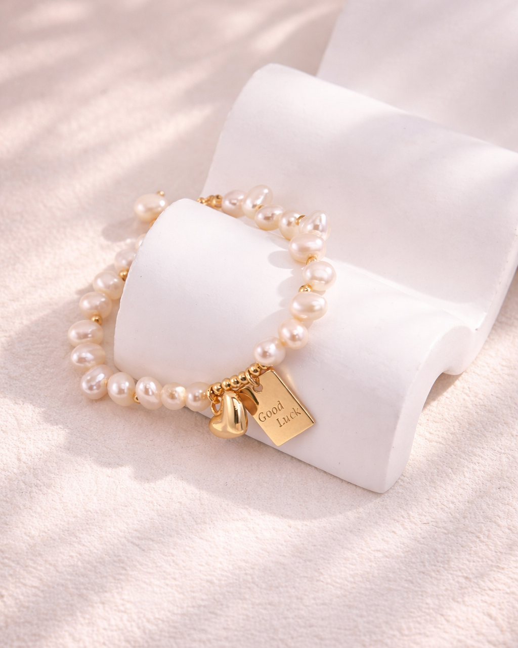 Freshwater pearl bracelet with gold heart charm and Good Luck pendant on a soft neutral background