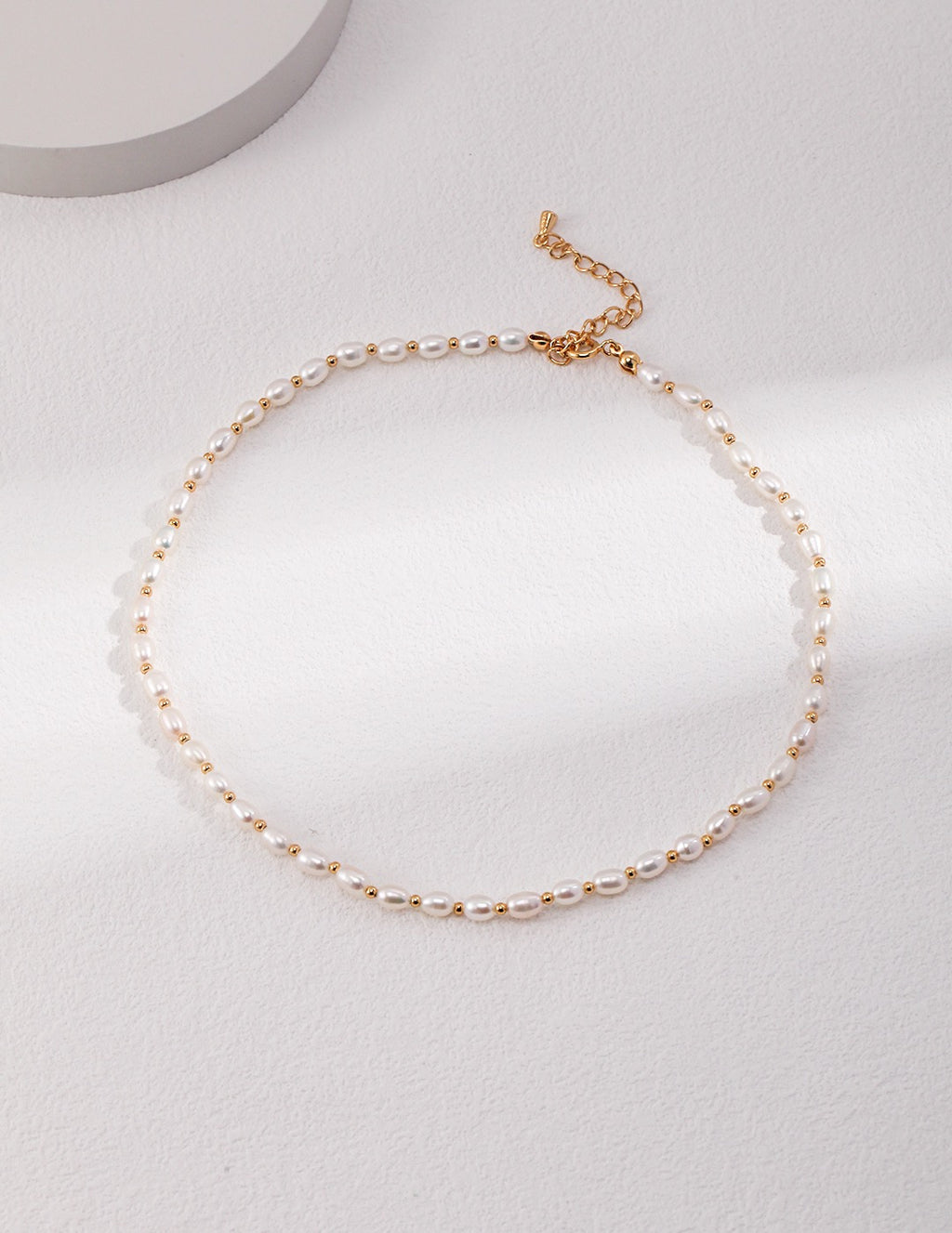 Minimalist freshwater pearl choker with gold accents displayed on soft white background