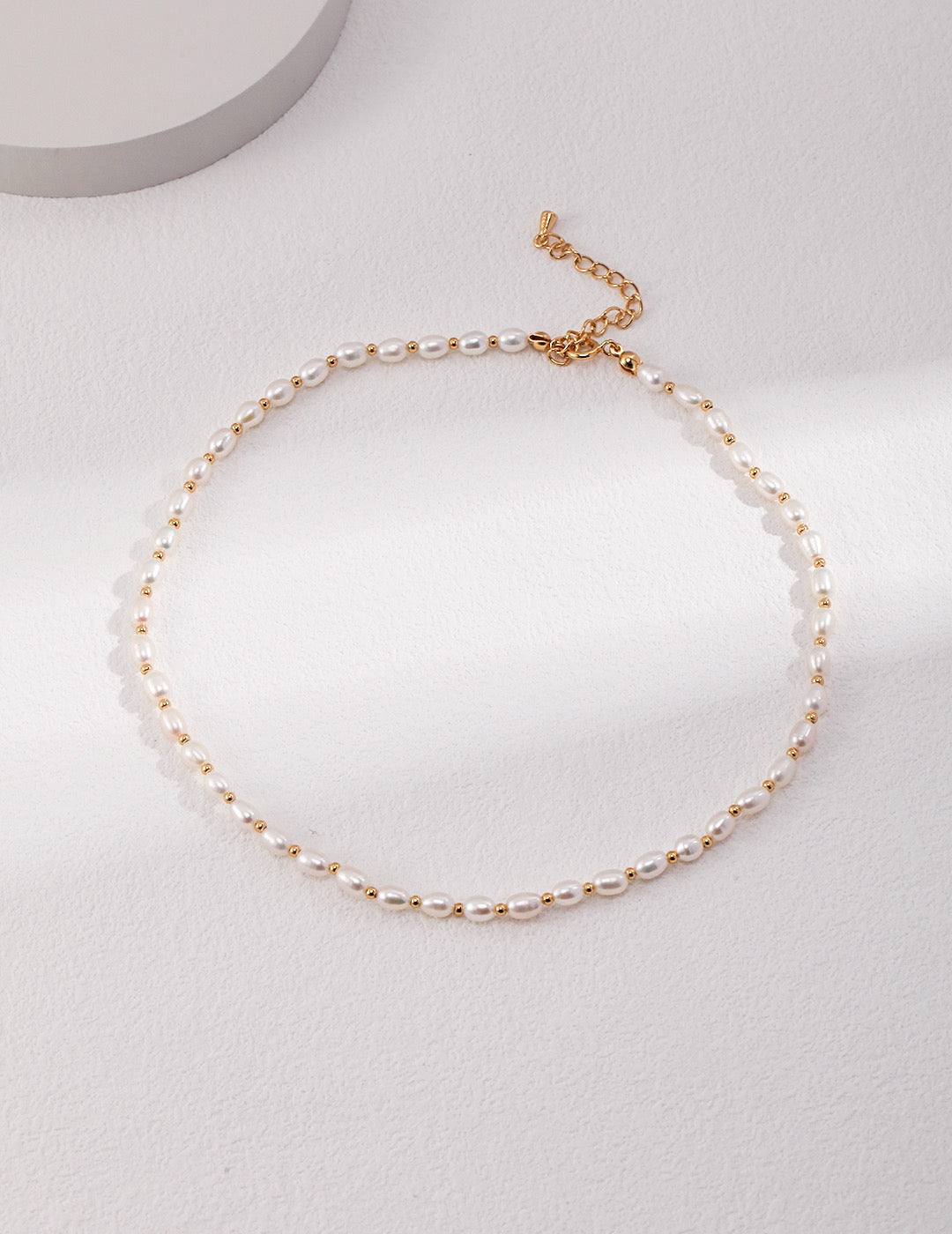Minimalist freshwater pearl choker with gold accents displayed on soft white background