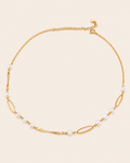 Minimalist gold chain necklace featuring freshwater pearls and elongated link details on a clean ivory background.