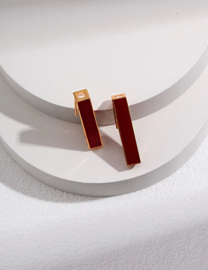 Minimalist gold rectangular drop earrings with red enamel bar and zircon accent on a white background