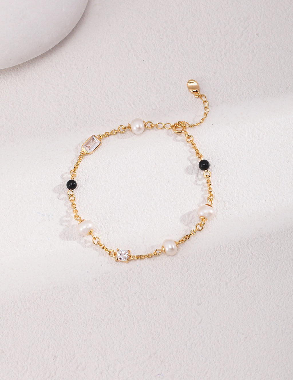 Elegant 18K gold plated bracelet with natural freshwater pearls, black onyx beads, and zircon stones on a white background