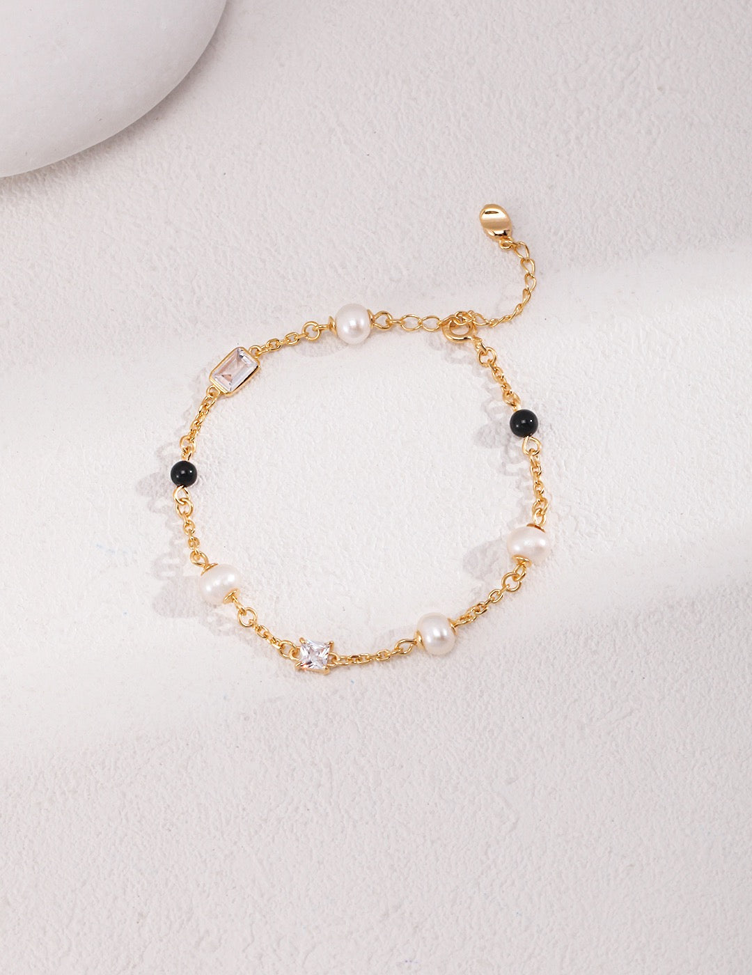 Elegant 18K gold plated bracelet with natural freshwater pearls, black onyx beads, and zircon stones on a white background