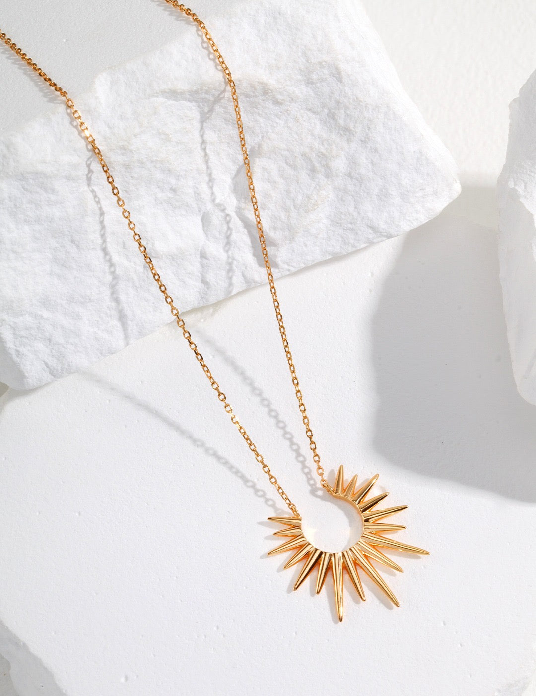 Gold sunburst pendant necklace on white stone background, 18K gold on 925 silver chain