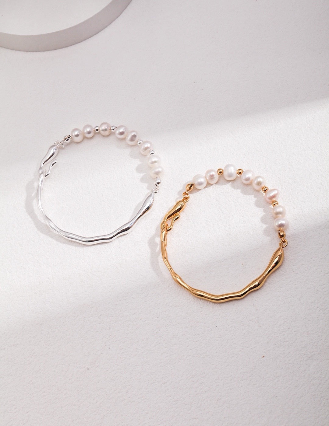 Wavy bracelet in 18K gold and 925 silver with natural freshwater pearls on a white background