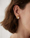 Vintage-inspired pearl stud earrings with textured gold fan design worn by model