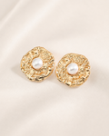 Vintage textured gold stud earrings with luminous pearl centers, showcased on a soft ivory fabric background for an elegant and timeless look.