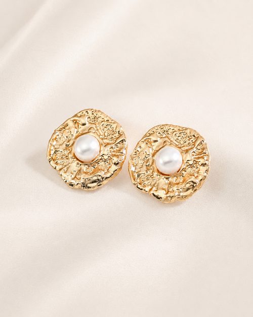 Vintage textured gold stud earrings with luminous pearl centers, showcased on a soft ivory fabric background for an elegant and timeless look.