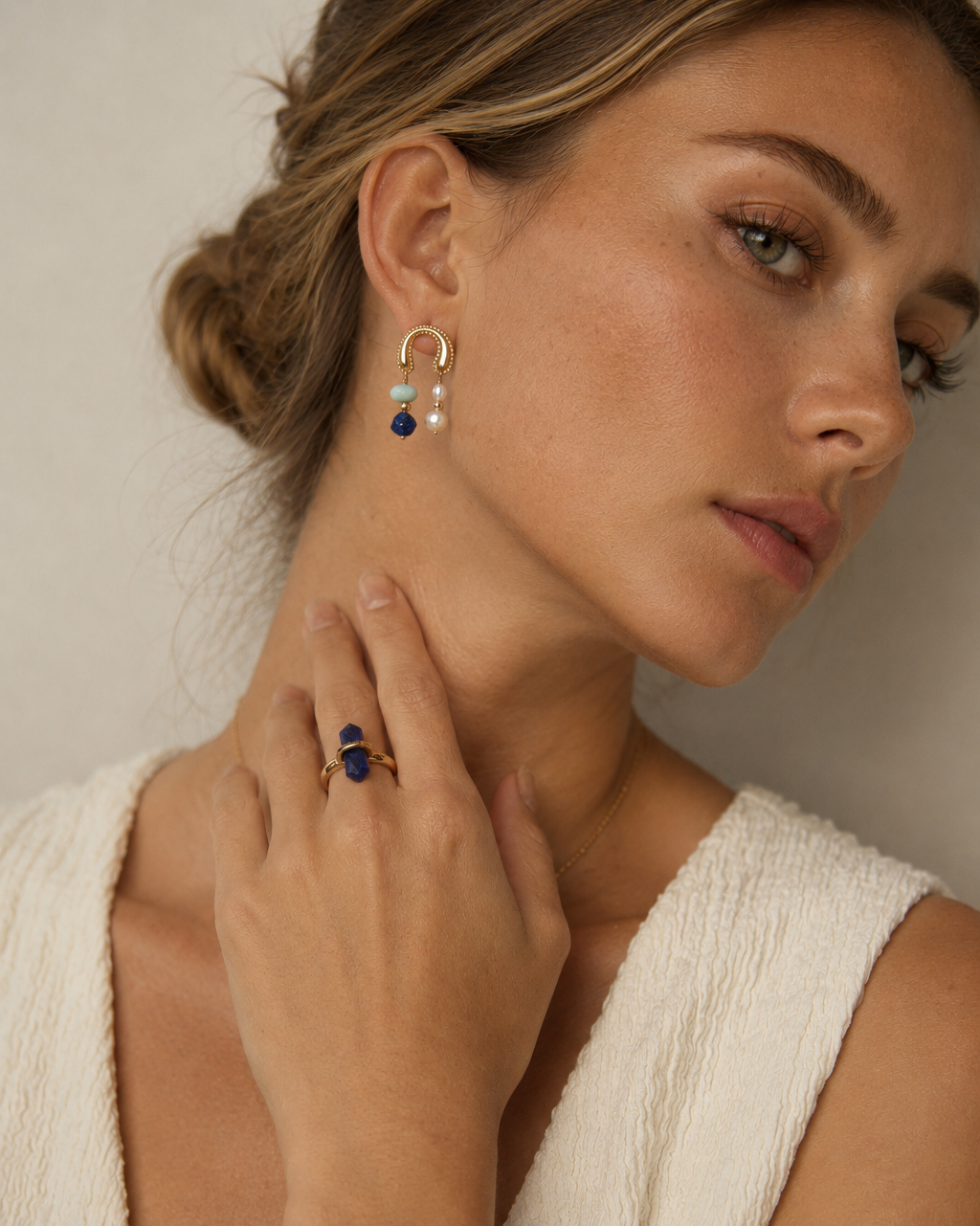 Close-up portrait of a European model wearing Celeste Arc Earrings in 18K gold vermeil with natural pearls and blue gemstone accents.