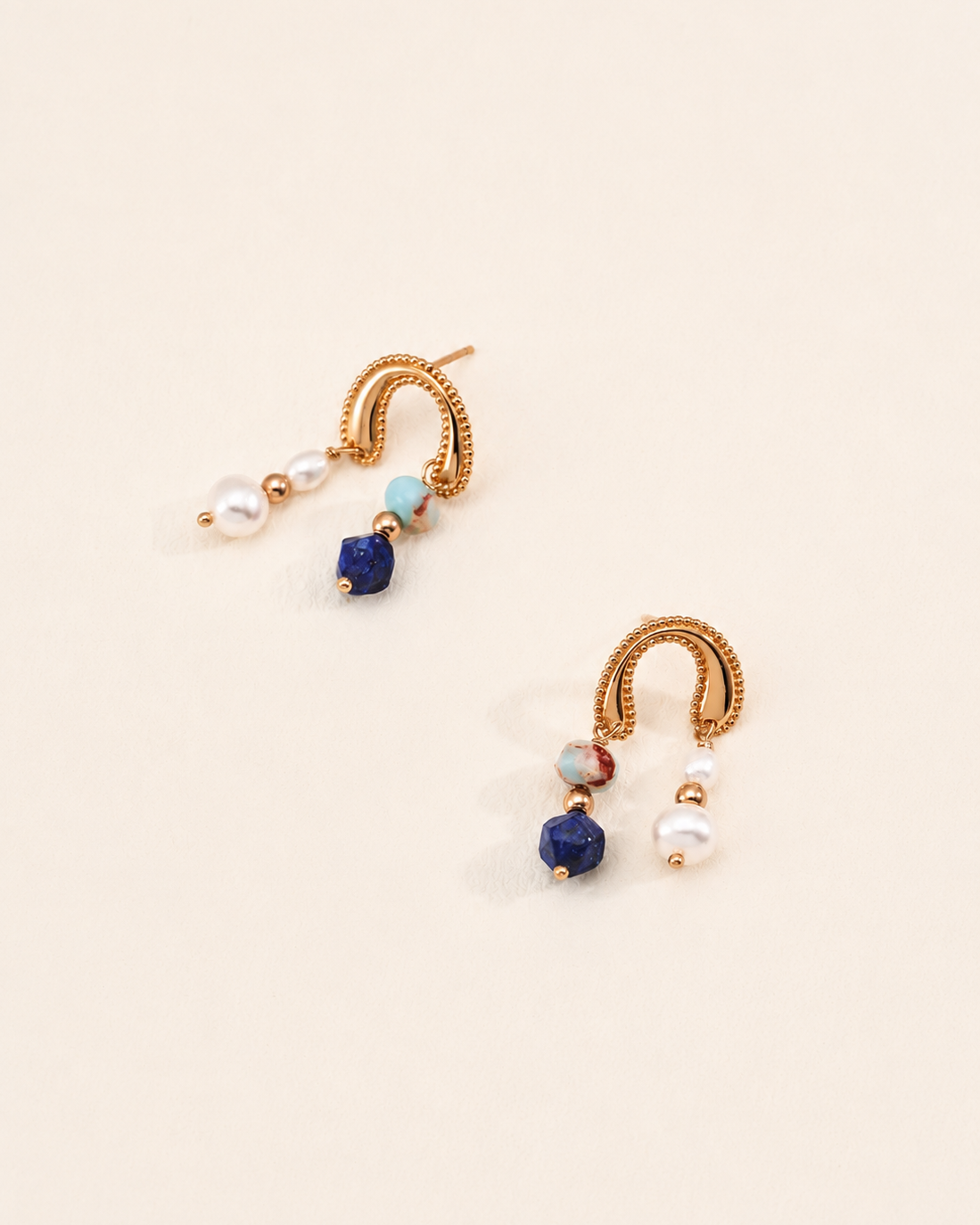 Flat lay of Celeste Arc Earrings crafted in 18K gold vermeil with freshwater pearls, lapis lazuli and Shoushan stone on a minimalist ivory background.