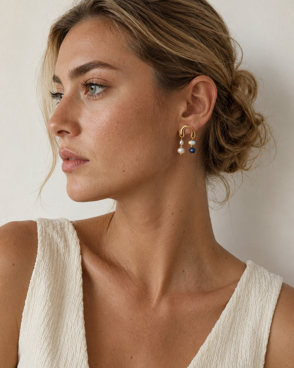 European model wearing Celeste Arc Earrings with freshwater pearls, lapis lazuli and Shoushan stone, shown in an elegant side-profile portrait.