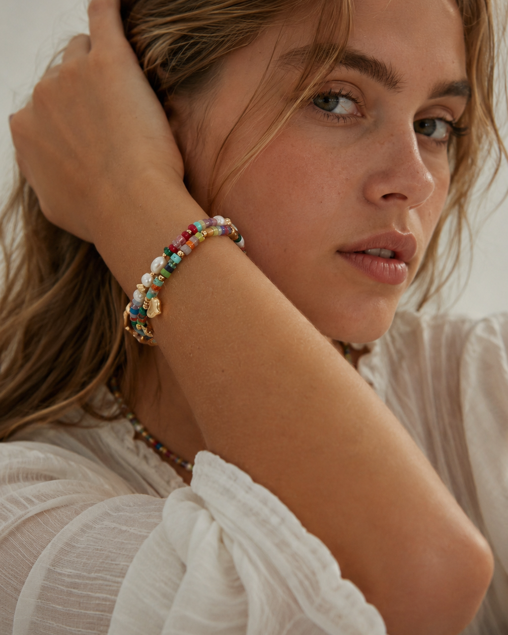 Model wearing a colorful natural gemstone bracelet with gold heart and star charms, styled for a relaxed summer look.
