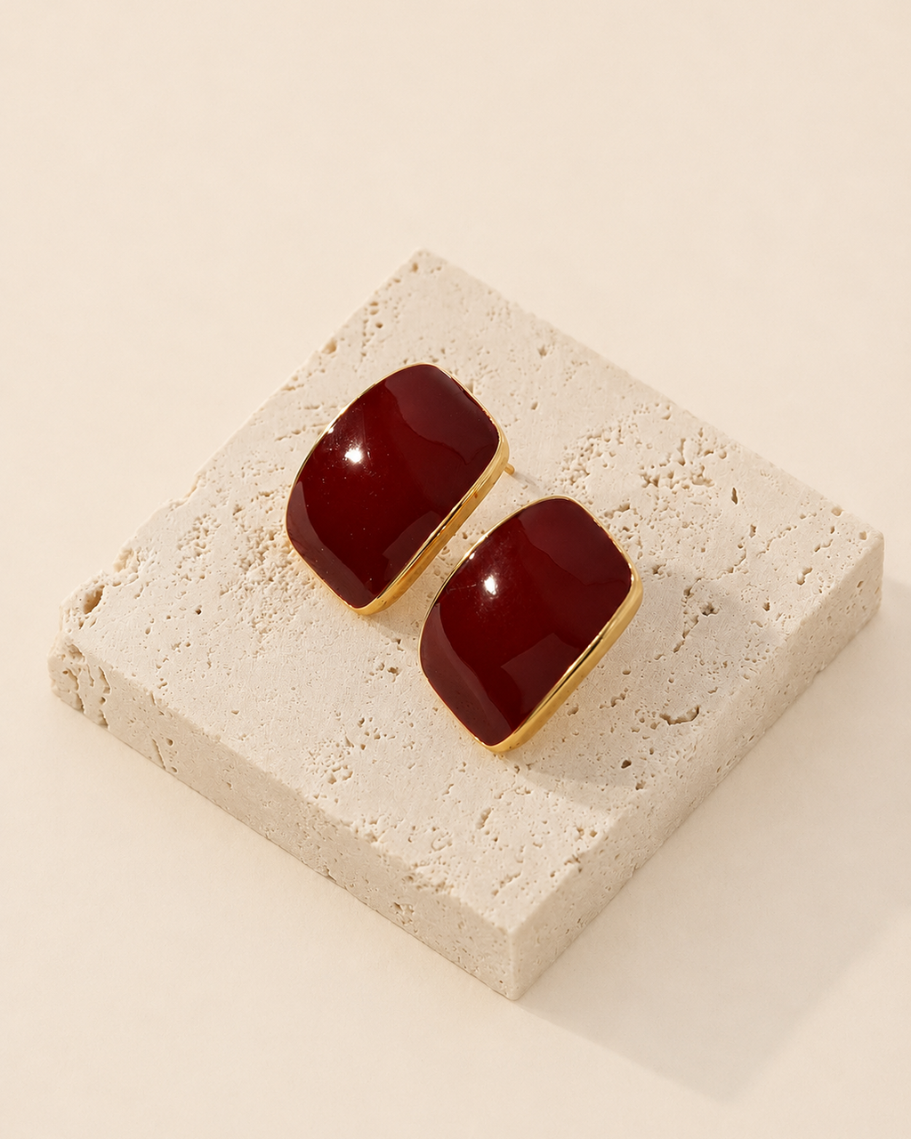 Burgundy enamel stud earrings crafted from S925 sterling silver with thick 18K gold plating, displayed on a natural travertine stone block.