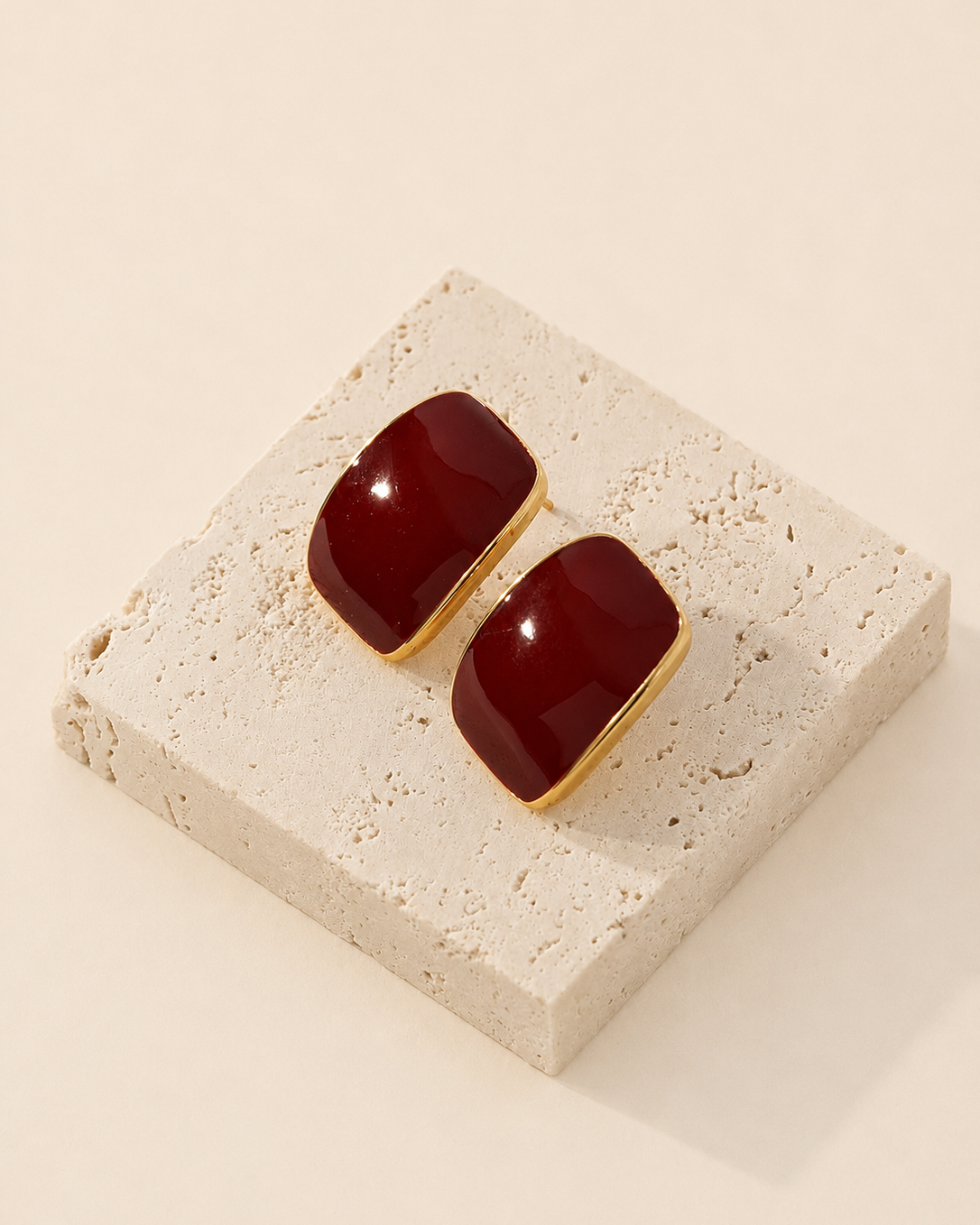 Burgundy enamel stud earrings crafted from S925 sterling silver with thick 18K gold plating, displayed on a natural travertine stone block.
