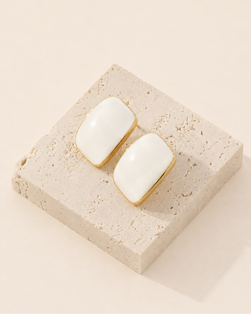 Ivory enamel stud earrings crafted from S925 sterling silver with thick 18K gold plating, displayed on a natural travertine stone block.