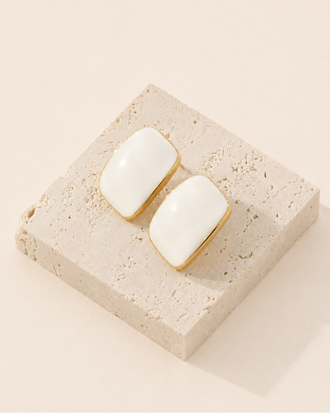Ivory enamel stud earrings crafted from S925 sterling silver with thick 18K gold plating, displayed on a natural travertine stone block.