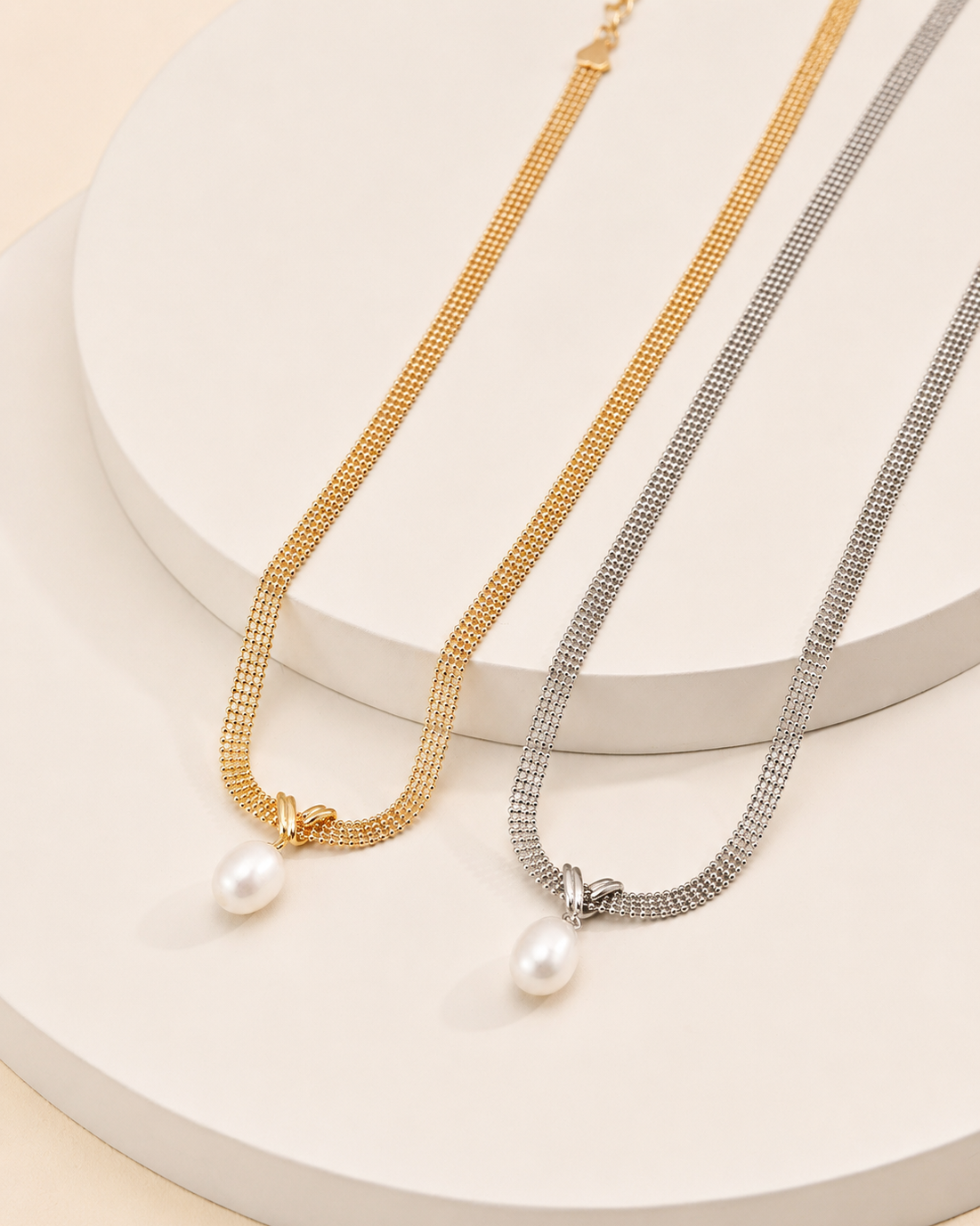 Gold and white gold mesh choker necklaces featuring natural freshwater pearl pendants displayed on a white pedestal.