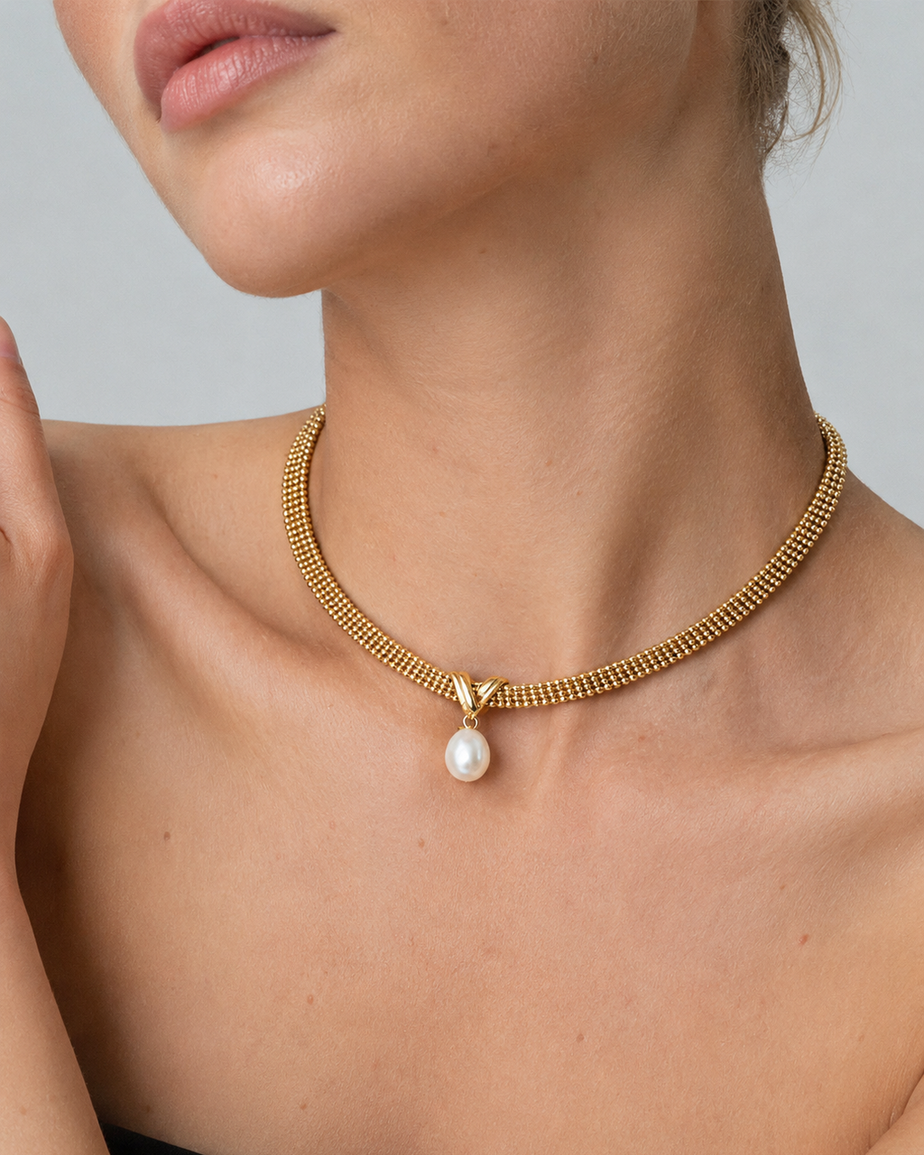 Woman wearing a gold mesh choker necklace featuring a natural freshwater pearl pendant.