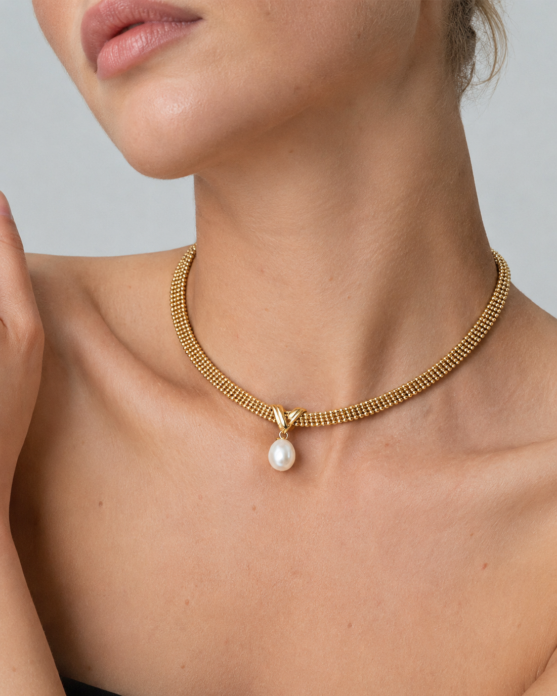 Woman wearing a gold mesh choker necklace featuring a natural freshwater pearl pendant.