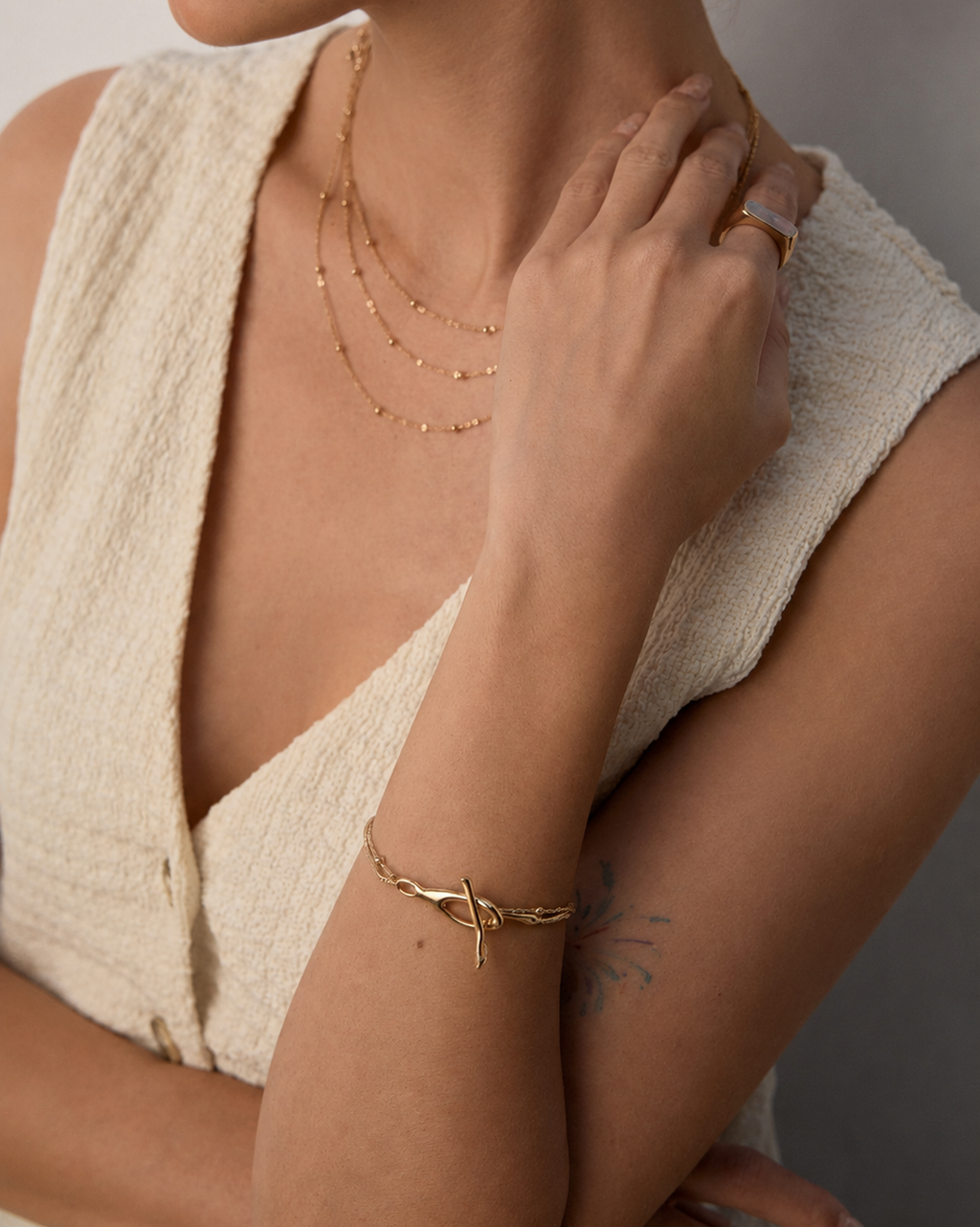 Model wearing a gold Entwine Branch bracelet with a modern organic clasp and layered chain details.