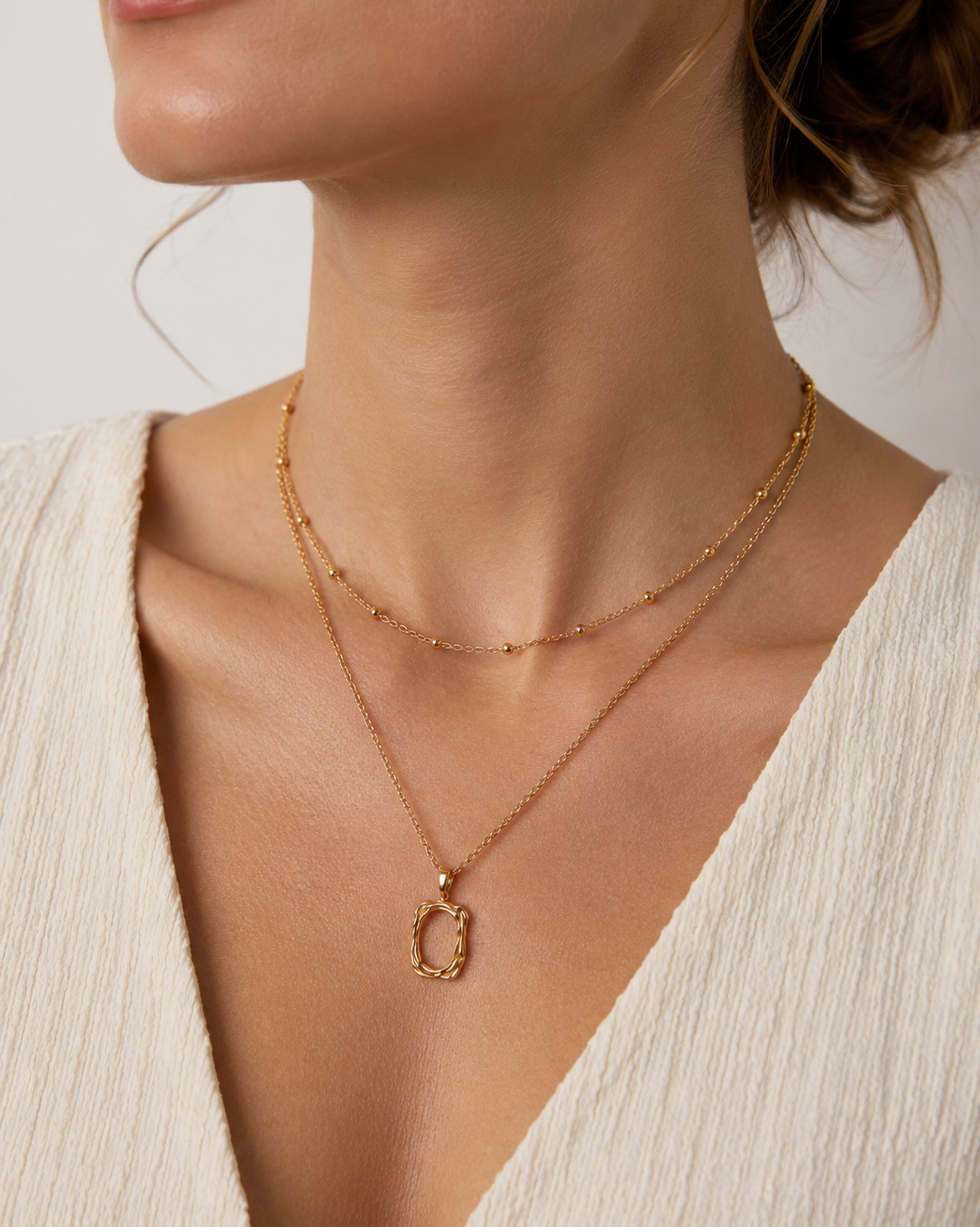 Close-up view of a gold plated organic frame pendant necklace on a woman's neckline, highlighting the sculptural pendant and delicate chain details.
