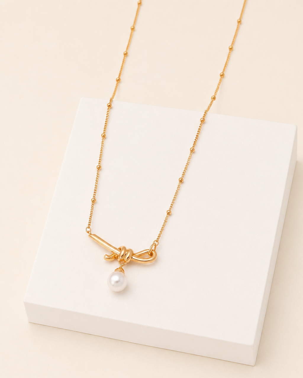 18k gold vermeil knot necklace with freshwater pearl pendant displayed on a modern white jewelry block.