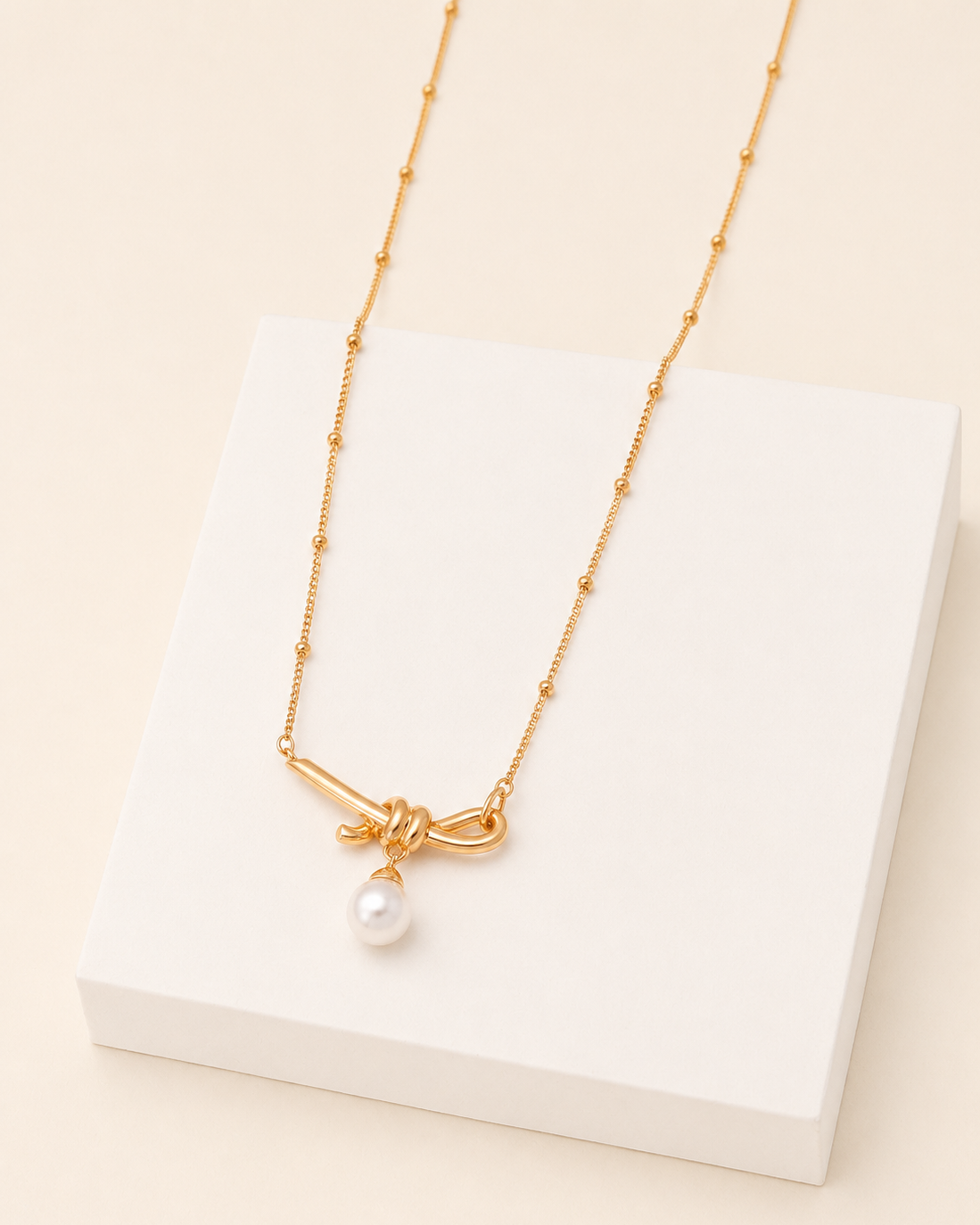 18k gold vermeil knot necklace with freshwater pearl pendant displayed on a modern white jewelry block.
