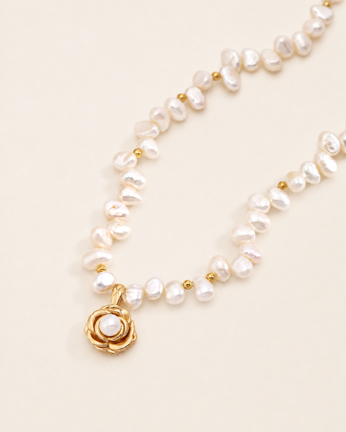 Close-up detail of a freshwater pearl necklace showcasing a gold camellia flower pendant with a lustrous pearl center and organically shaped pearls.