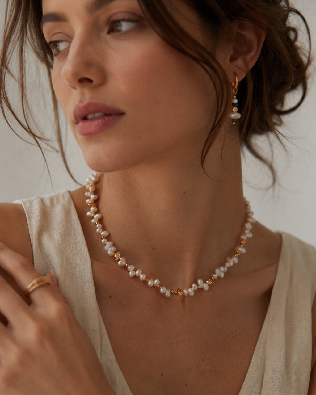 Freshwater pearl necklace with organic gold bead accents displayed on a textured white stone pedestal, elegant coastal-inspired jewelry in 18K gold plated sterling silver.