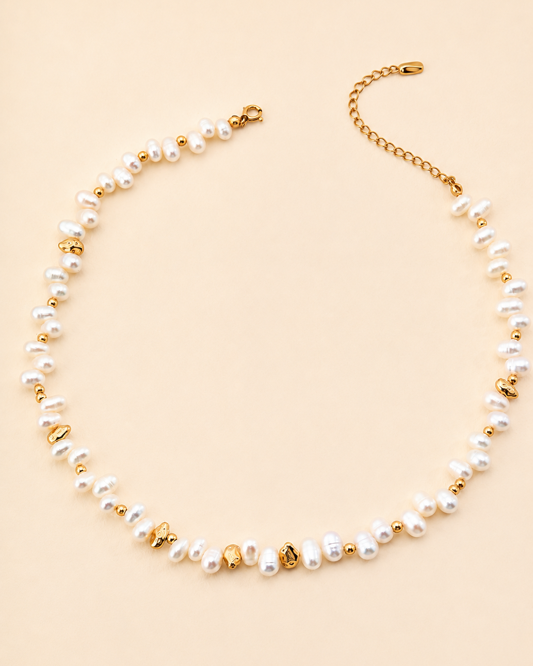 Freshwater pearl necklace with organic gold bead accents displayed on a soft beige background, featuring irregular pearls and adjustable extension chain.