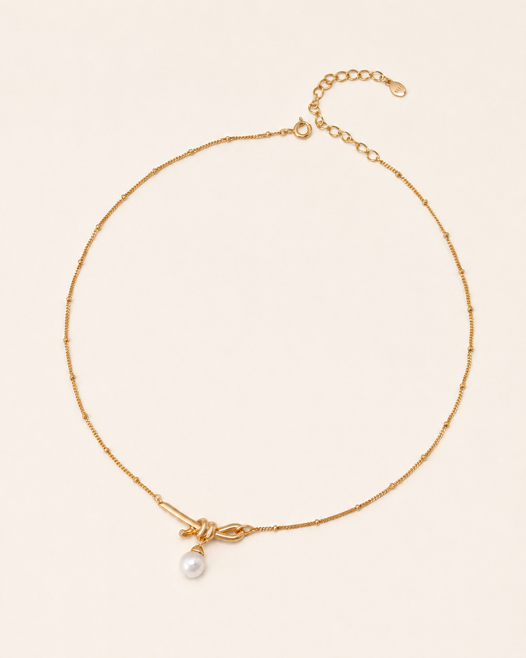 Minimalist gold knot necklace featuring a freshwater pearl pendant on a delicate beaded chain with adjustable length.