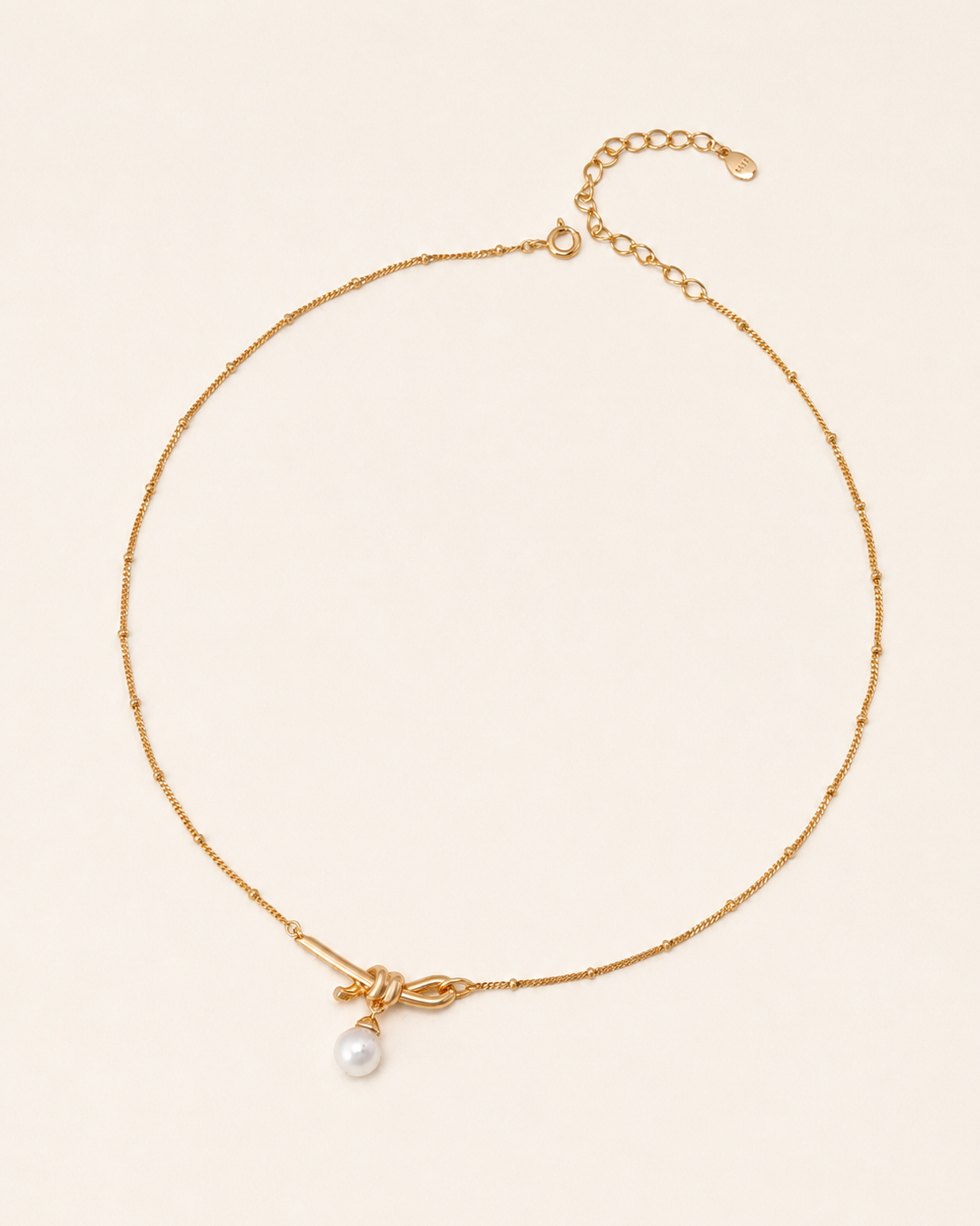 Minimalist gold knot necklace featuring a freshwater pearl pendant on a delicate beaded chain with adjustable length.