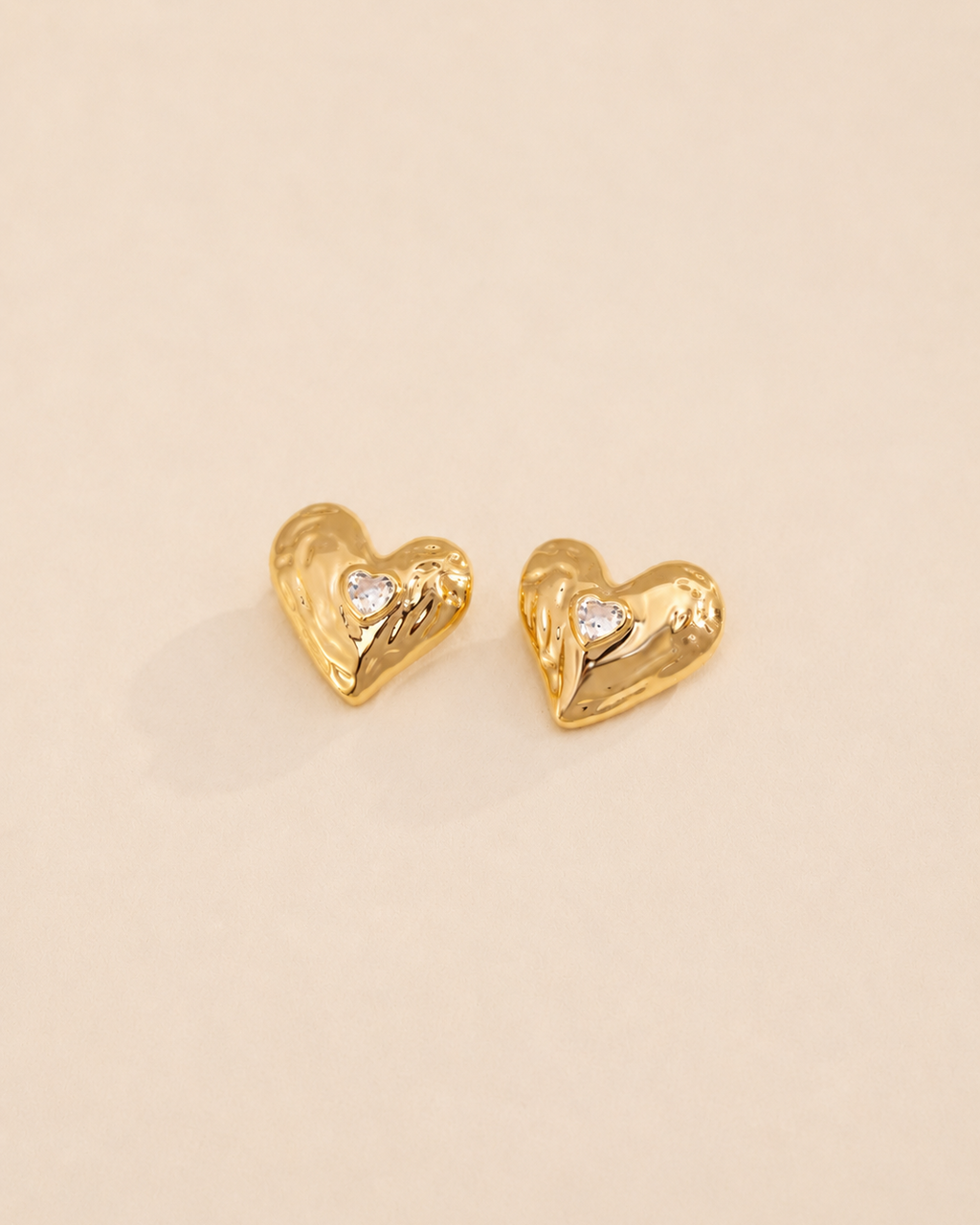 Lumi Heart Stud Earrings in thick 18K gold plated S925 sterling silver with heart-shaped cubic zirconia on a soft ivory background.