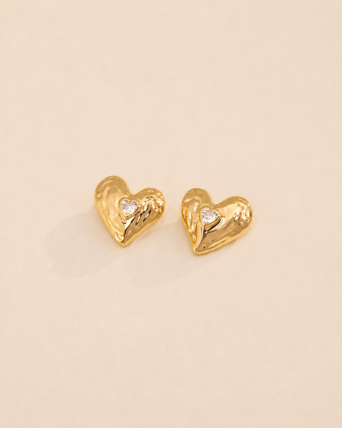 Lumi Heart Stud Earrings in thick 18K gold plated S925 sterling silver with heart-shaped cubic zirconia on a soft ivory background.