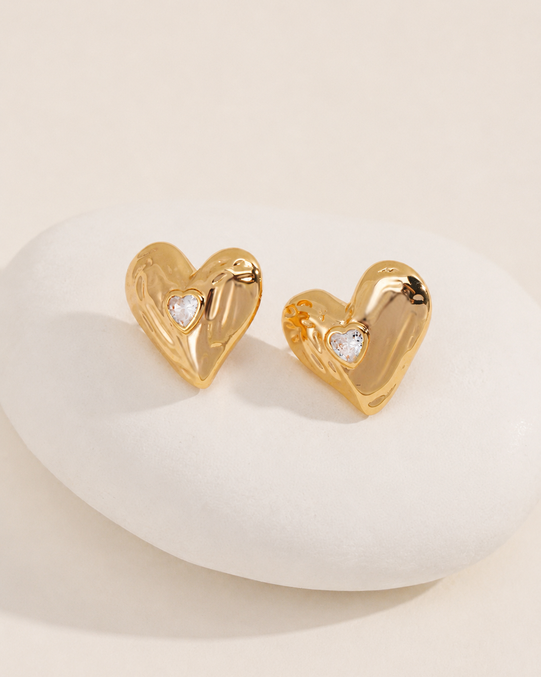 Lumi Heart Stud Earrings crafted from S925 sterling silver with thick 18K gold plating and heart-cut cubic zirconia displayed on a white stone pedestal.