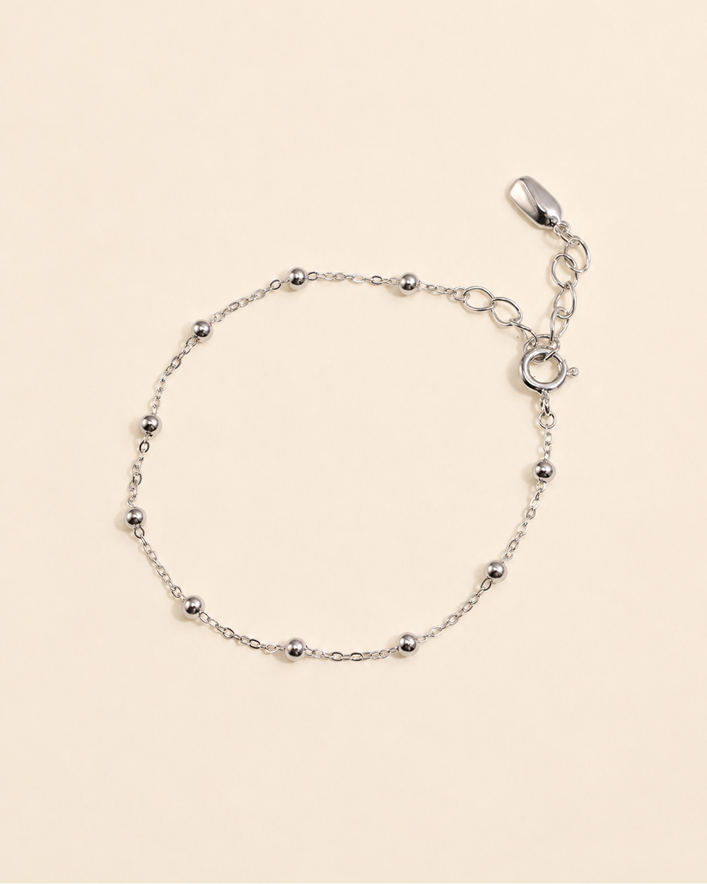 Minimalist white gold plated satellite chain bracelet with polished bead details on a soft cream background.