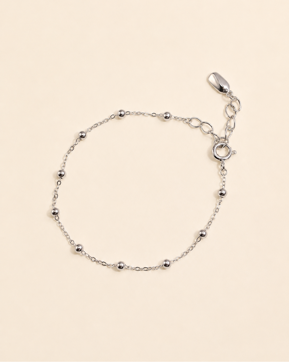 Minimalist white gold plated satellite chain bracelet with polished bead details on a soft cream background.