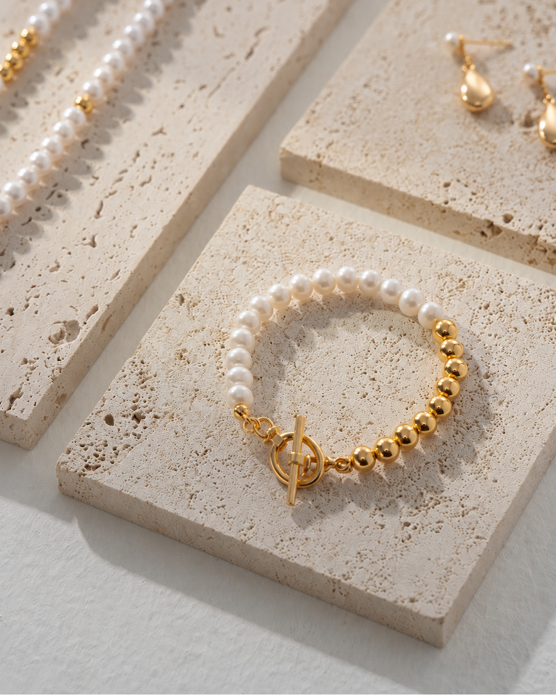 Luna Pearl T-Bar Bracelet featuring natural freshwater pearls and thick 18K gold plated sterling silver displayed on a textured stone surface.