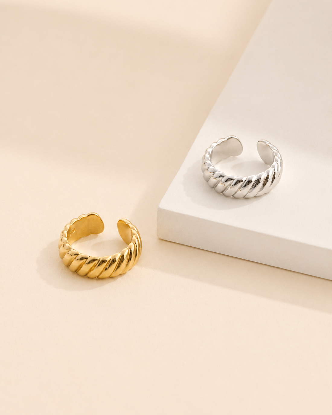 Adjustable rope texture ring available in thick 18K gold and thick 18K white gold plated finishes on an ivory display.