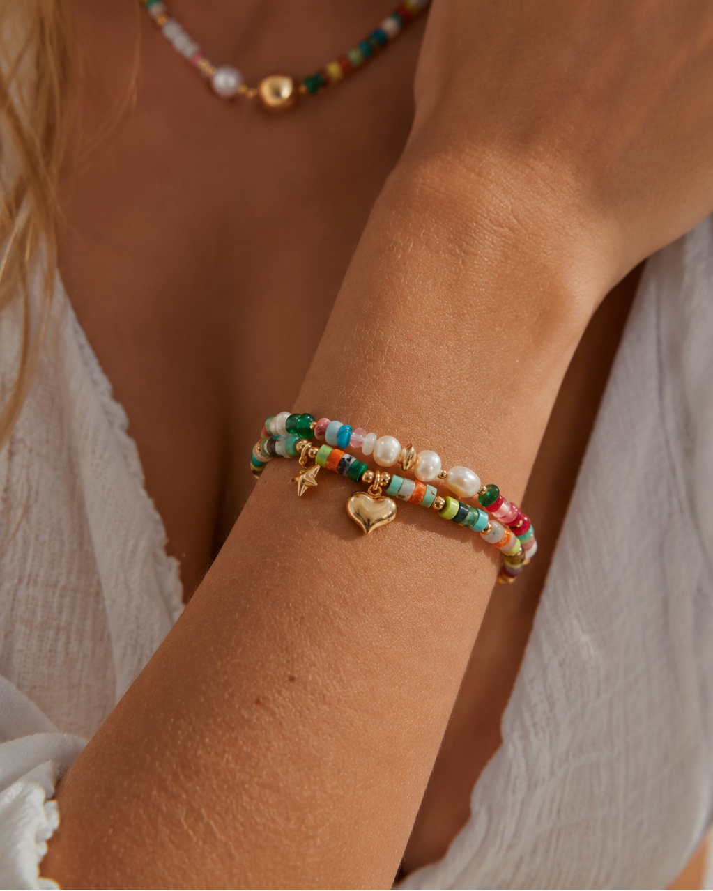 Close-up of a colorful gemstone beaded bracelet featuring gold heart and star charms, worn on the wrist.