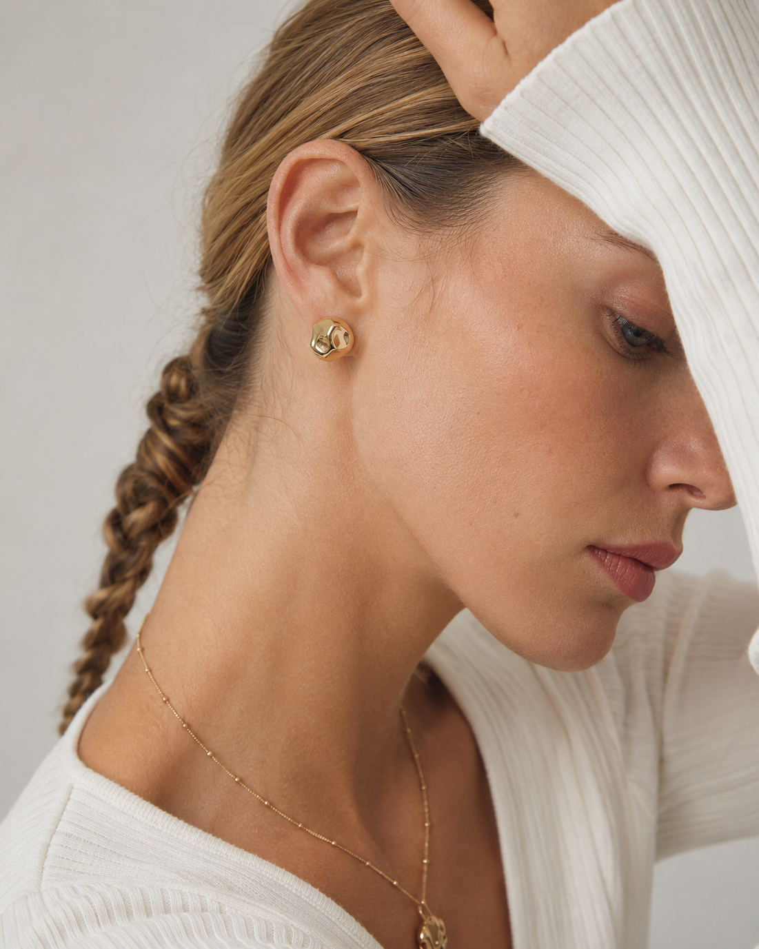 Close-up of a model wearing organic gold stud earrings in thick 18K gold plating, highlighting the sculptural pebble-inspired design and polished finish.