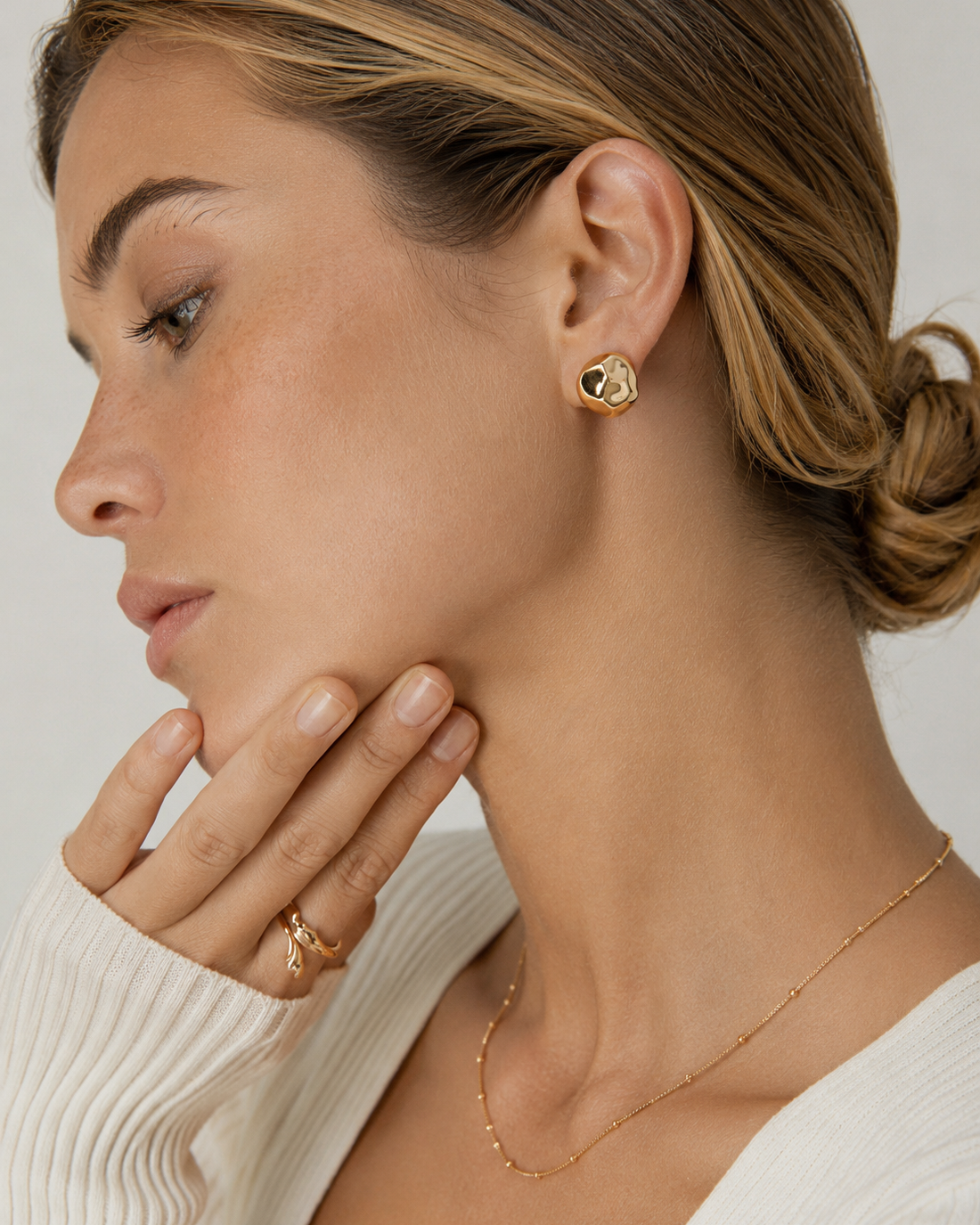 Model wearing organic gold stud earrings in thick 18K gold plating, featuring a sculptural pebble-inspired design with a modern minimalist look.