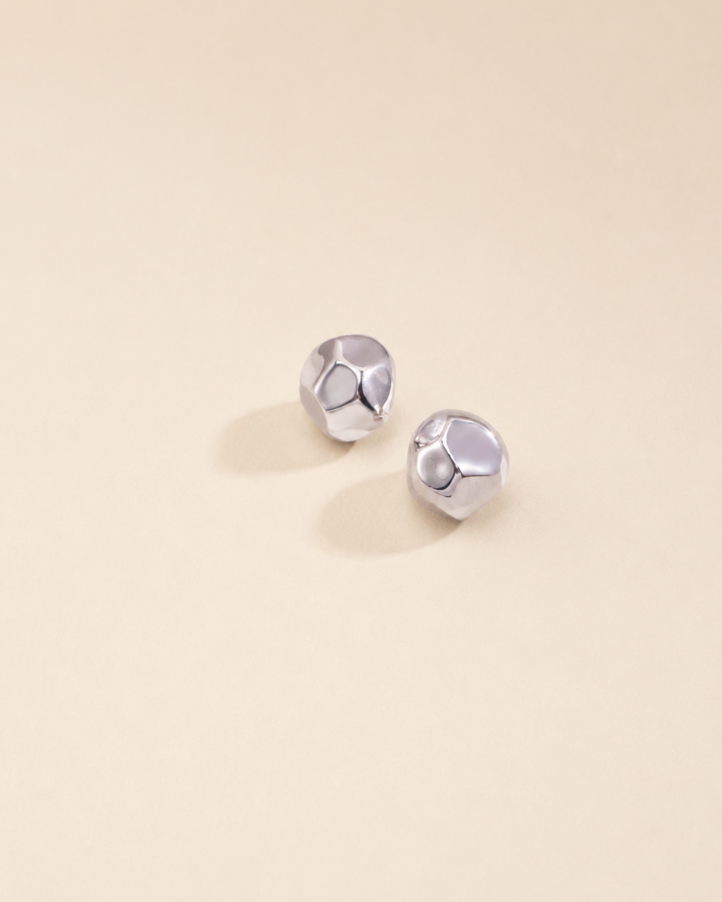 Organic silver stud earrings in thick 18K white gold plating with a sculptural pebble-inspired design on a soft beige background.