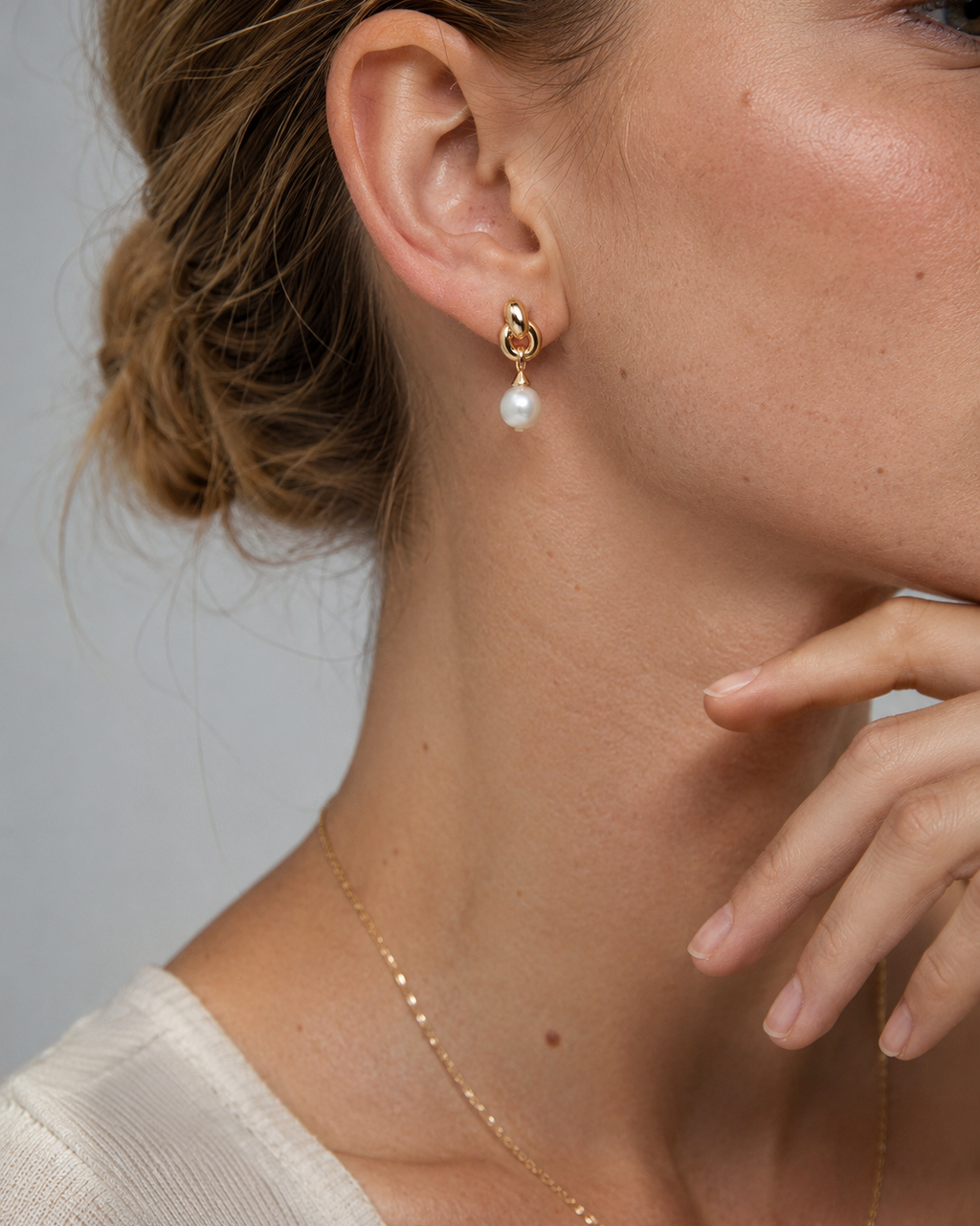 Close-up of NORA Pearl Earrings featuring gold knot links with a freshwater pearl drop on a model's ear