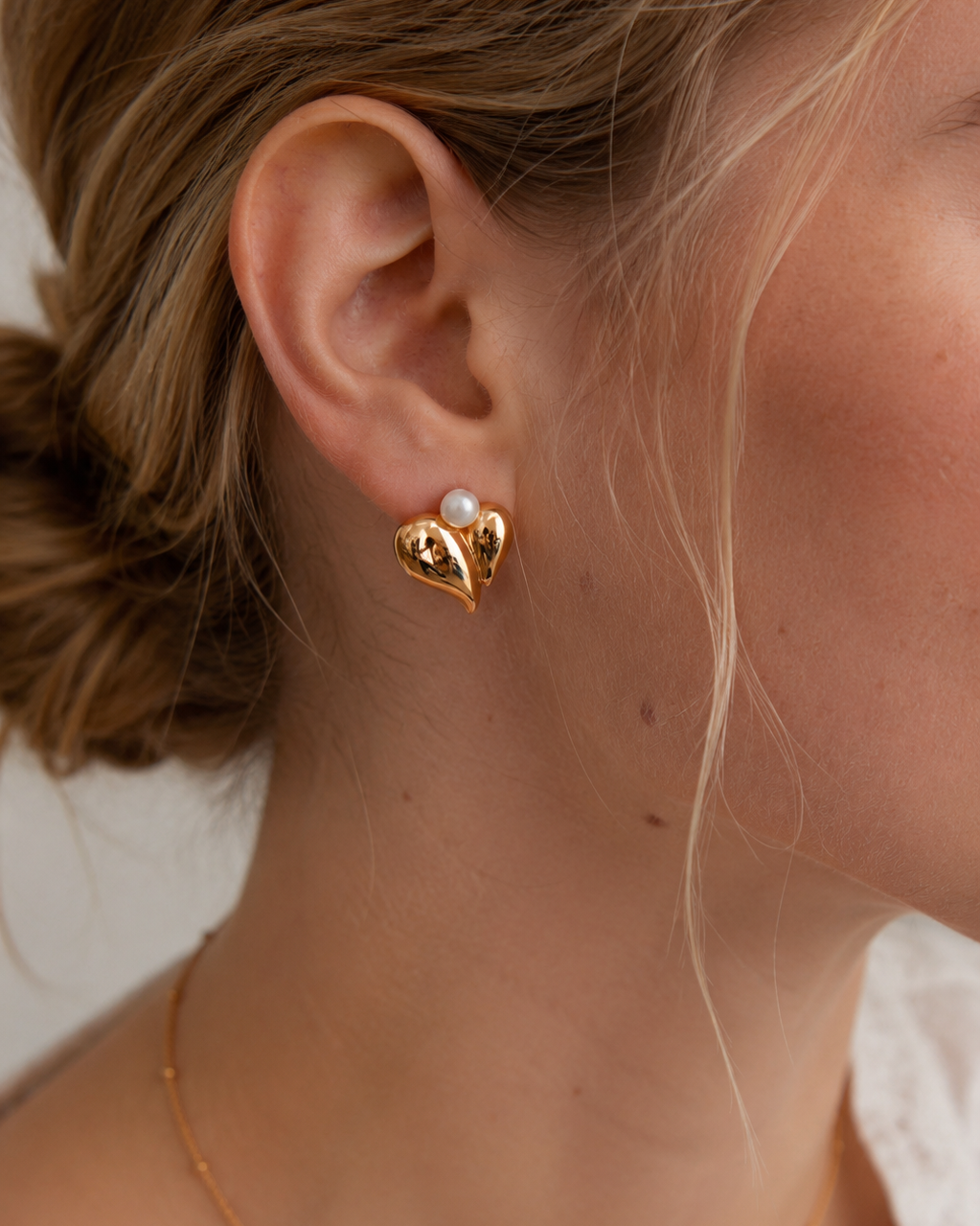 Close-up of vintage gold pearl heart stud earrings with natural freshwater pearls worn on ear.