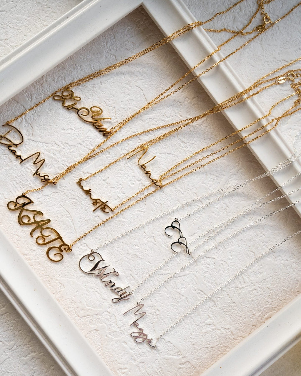Personalized script name necklaces in gold and silver on textured neutral background